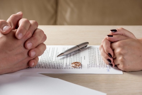 A couple sitting at a table with a divorce agreement and wedding rings